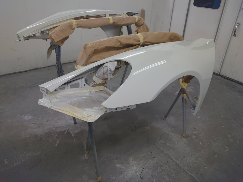 the front fender of a white porsche car is being painted in a car body repair garage in cardiff city, south wales